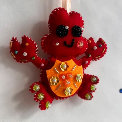 Cangrejito rojo con barriga naranja, sonrisa bordada y piedritas en las patas.