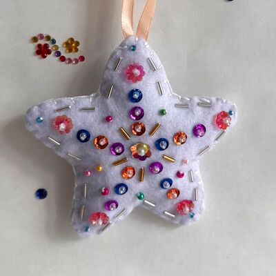 Estrella blanca colgada de una cinta, con lentejuelas de colores y canutillos dorados.
