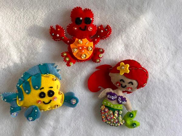 El set Bajo el mar sobre una cobija blanca: un cangrejito rojo, un pececito amarillo con aletas turquesa y una sirenita de pelo rojo.