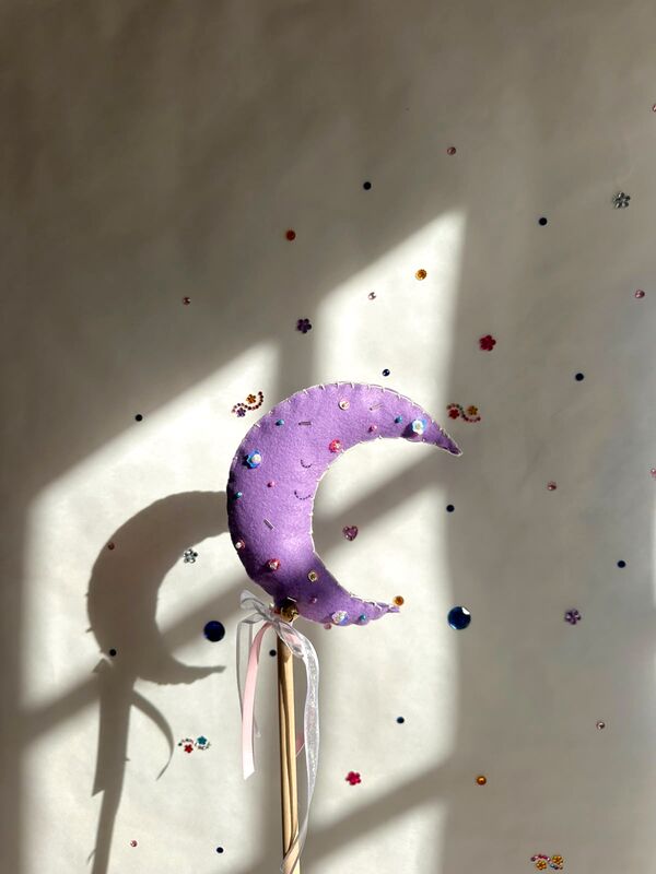 Varita mágica: una luna lila con perlitas, en un palito de madera con cintas, a la luz de la ventana.